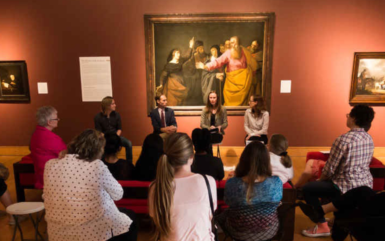 Dr. Alexander Rich and others gathered in a gallery room discussing artworks in a seated group setting.