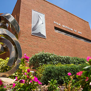 Exterior of Polk Museum of Art building with metal sculpture and pink flowers in frame.