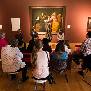 Dr. Alexander Rich and others gathered in a gallery room discussing artworks in a seated group setting.