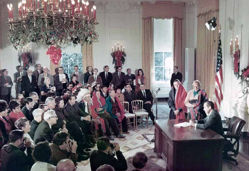 President Nixon signing a bill in front of an audience including politicians, as well as Native Americans in traditional dress
