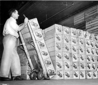 A man dropping off a stack of crates on a dolly